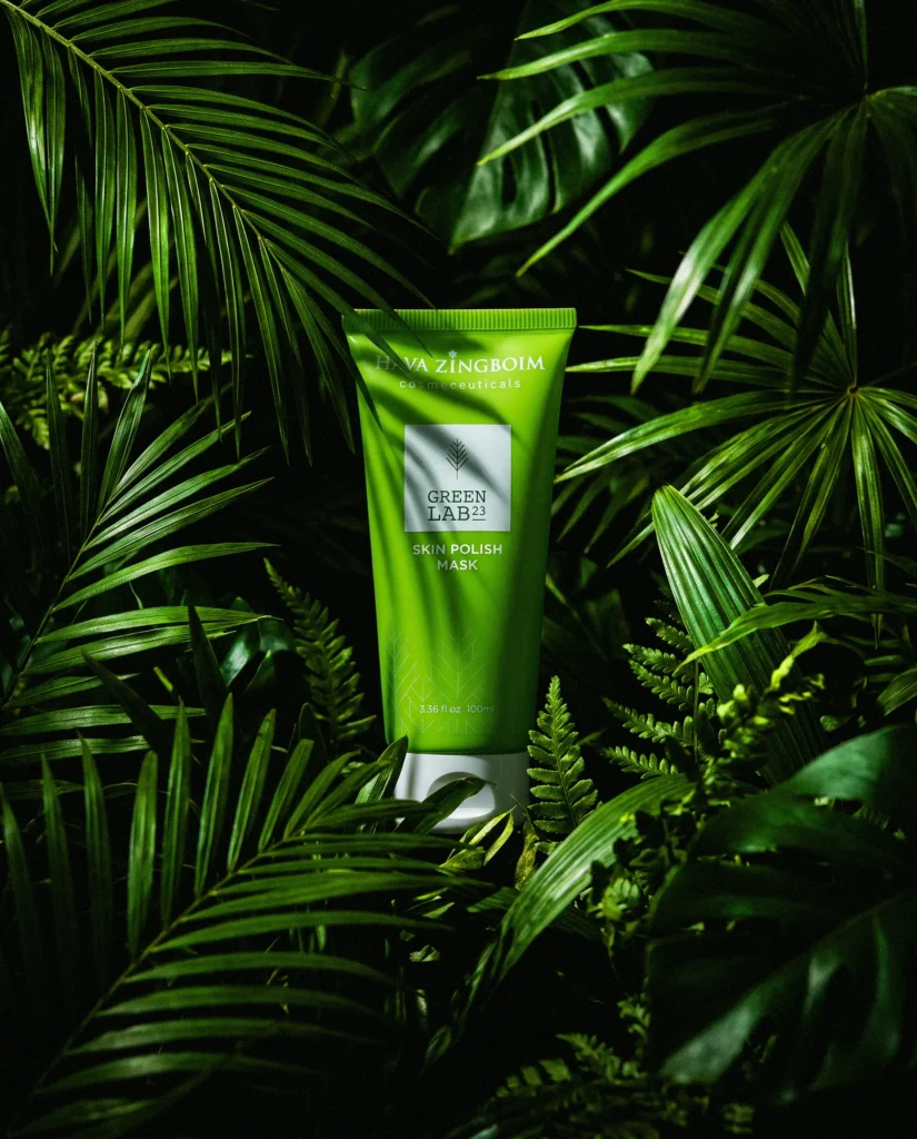 Green skincare tube among tropical palm and fern leaves