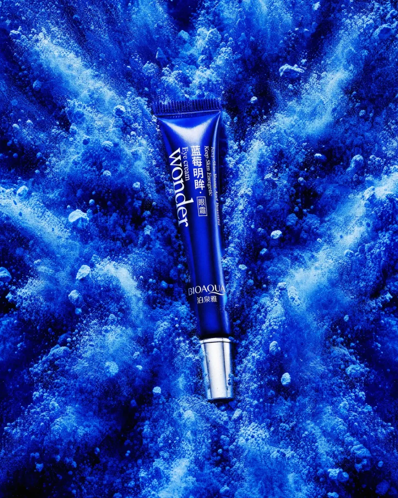 Blue eye-cream tube in a swirl of blue powder and ice