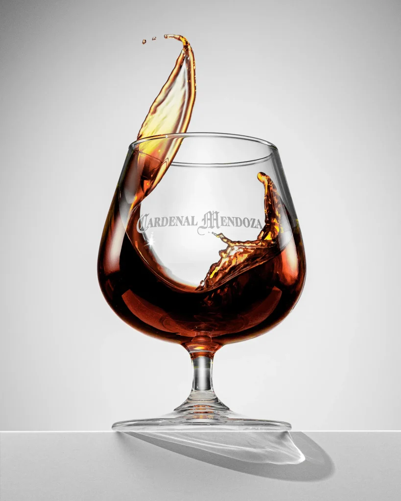Brandy swirling out of a balloon glass against a pale grey backdrop
