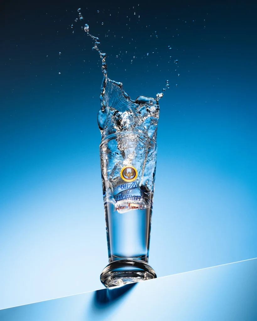 Lager splashing upward from a tall footed beer glass on blue