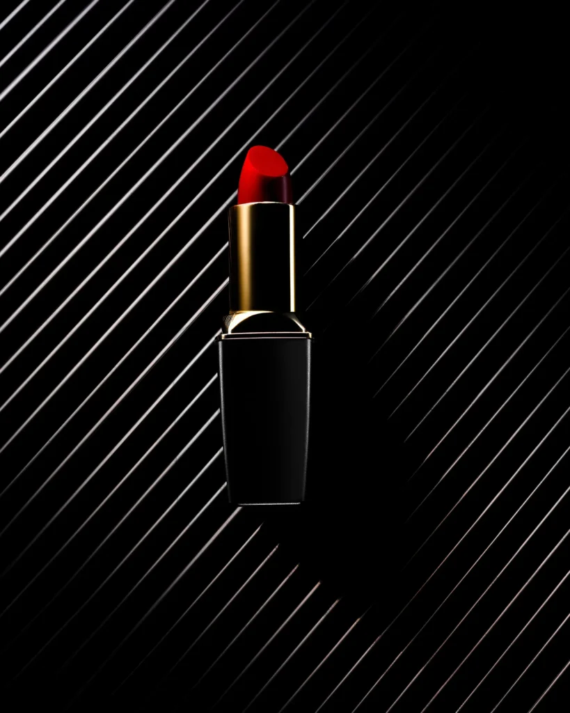 Red lipstick bullet on a black surface raked with diagonal light
