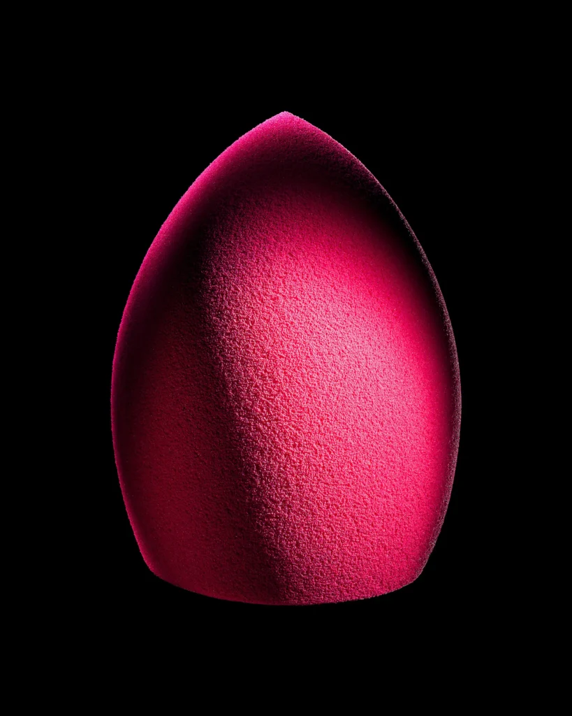 Magenta teardrop makeup sponge lit against black
