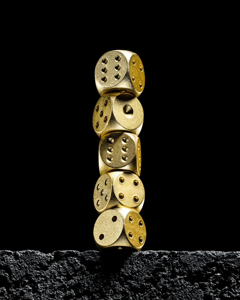 Stack of five gold dice balanced on black volcanic rock
