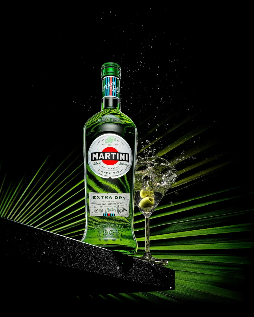 Green vermouth bottle and cocktail glass over a lit palm frond