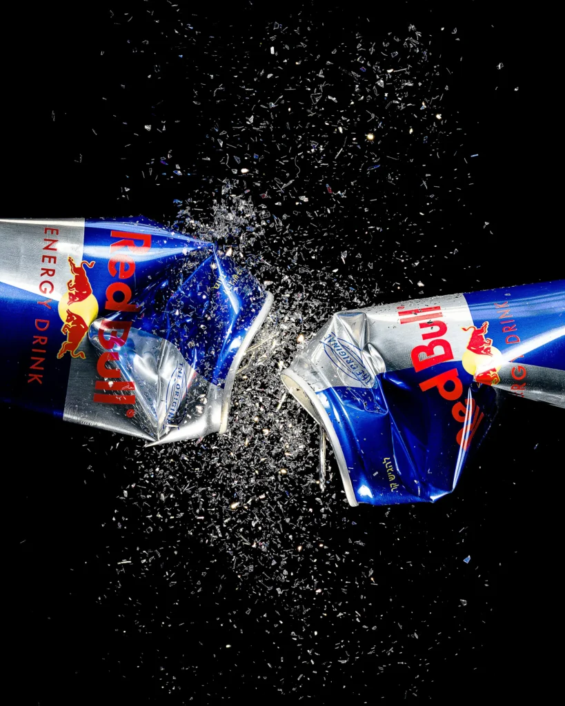 Two crushed energy-drink cans exploding in dark grit