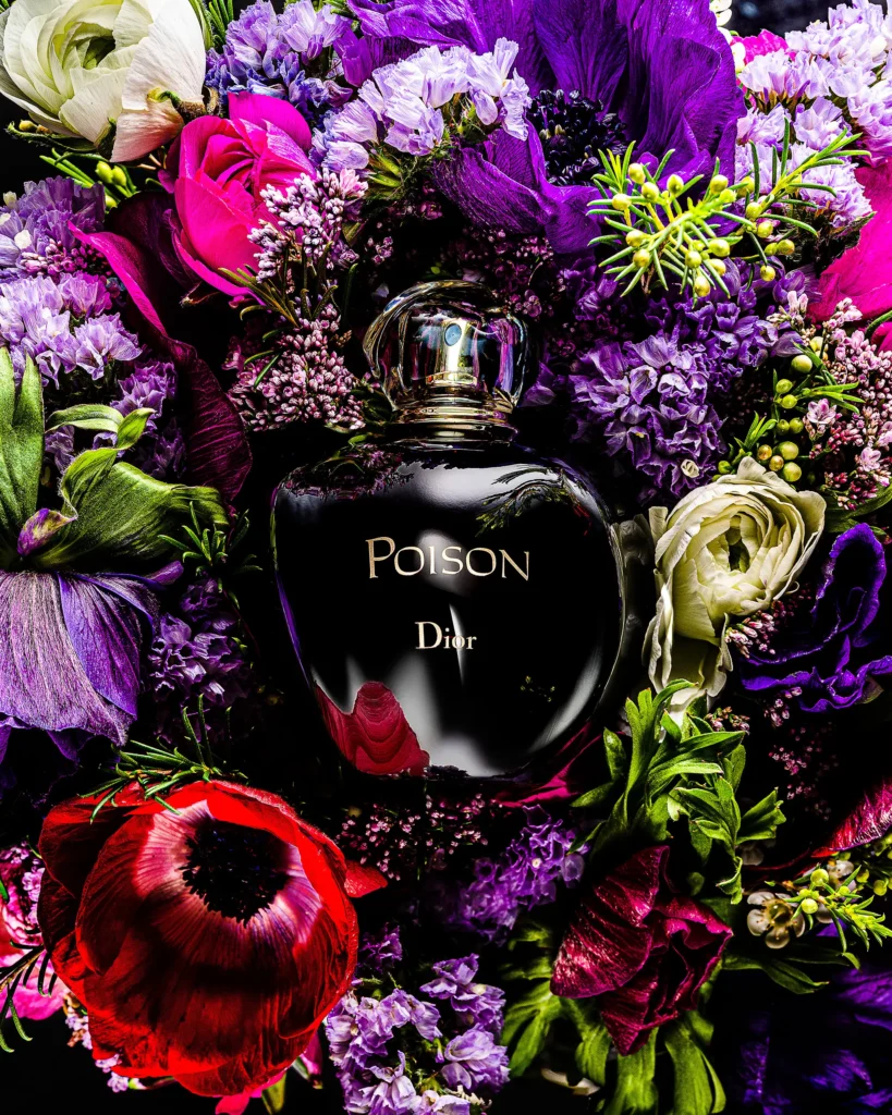 Dark perfume flask set into a dense bouquet of purple and red flowers