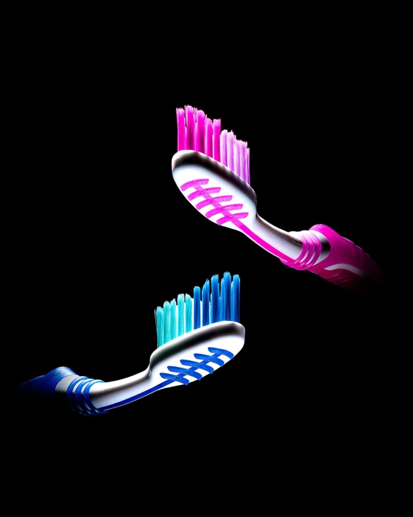 Pink and blue toothbrushes crossing in mid-air on black