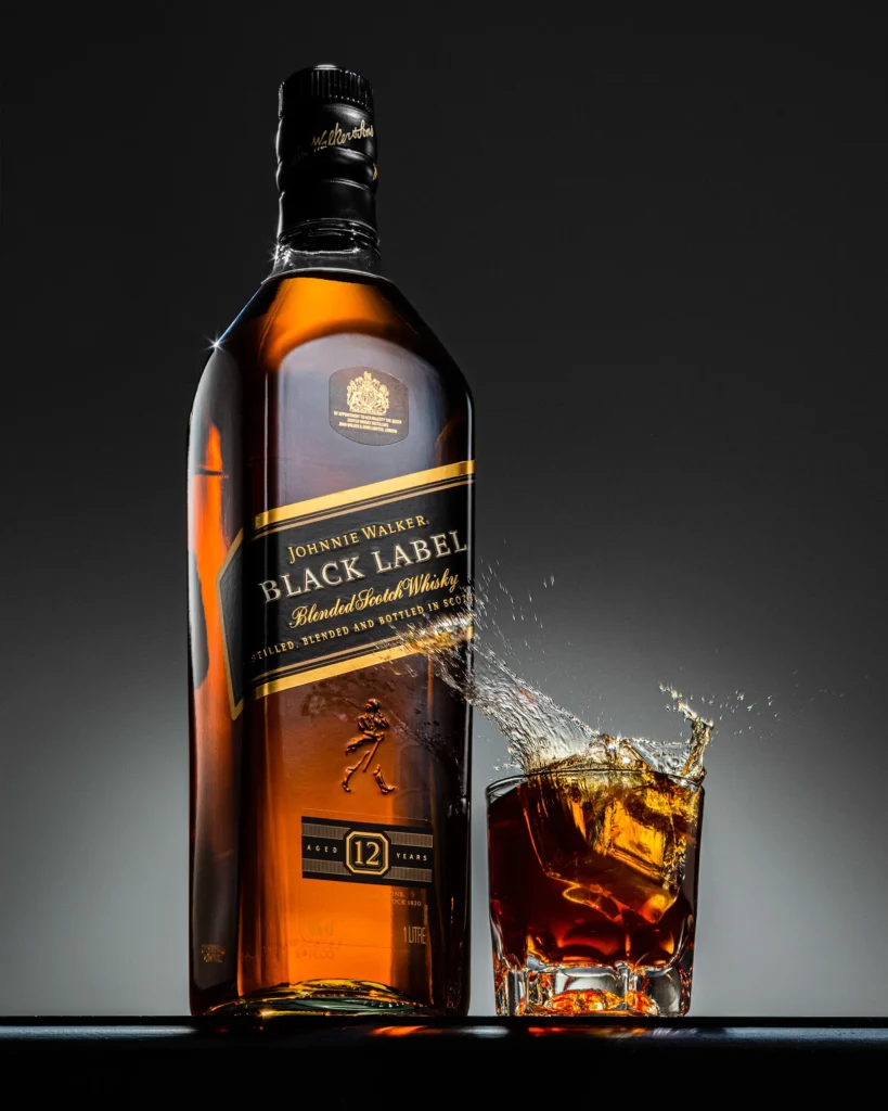 Whisky bottle beside a tumbler with liquid splashing