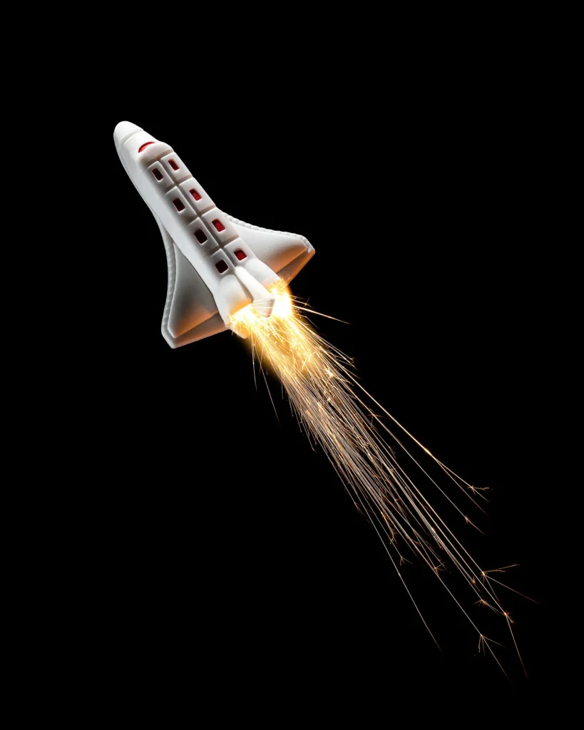 Toy space shuttle trailing sparks against black