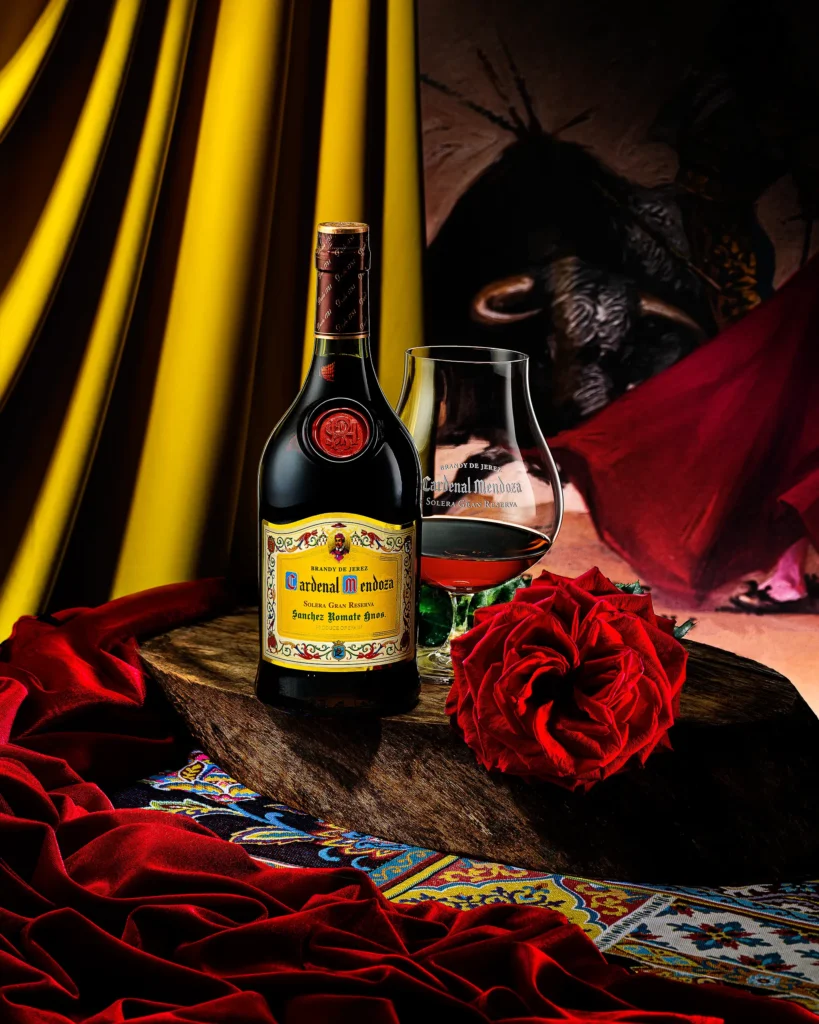 Brandy bottle and glass in a still life with velvet, rose and patterned tile
