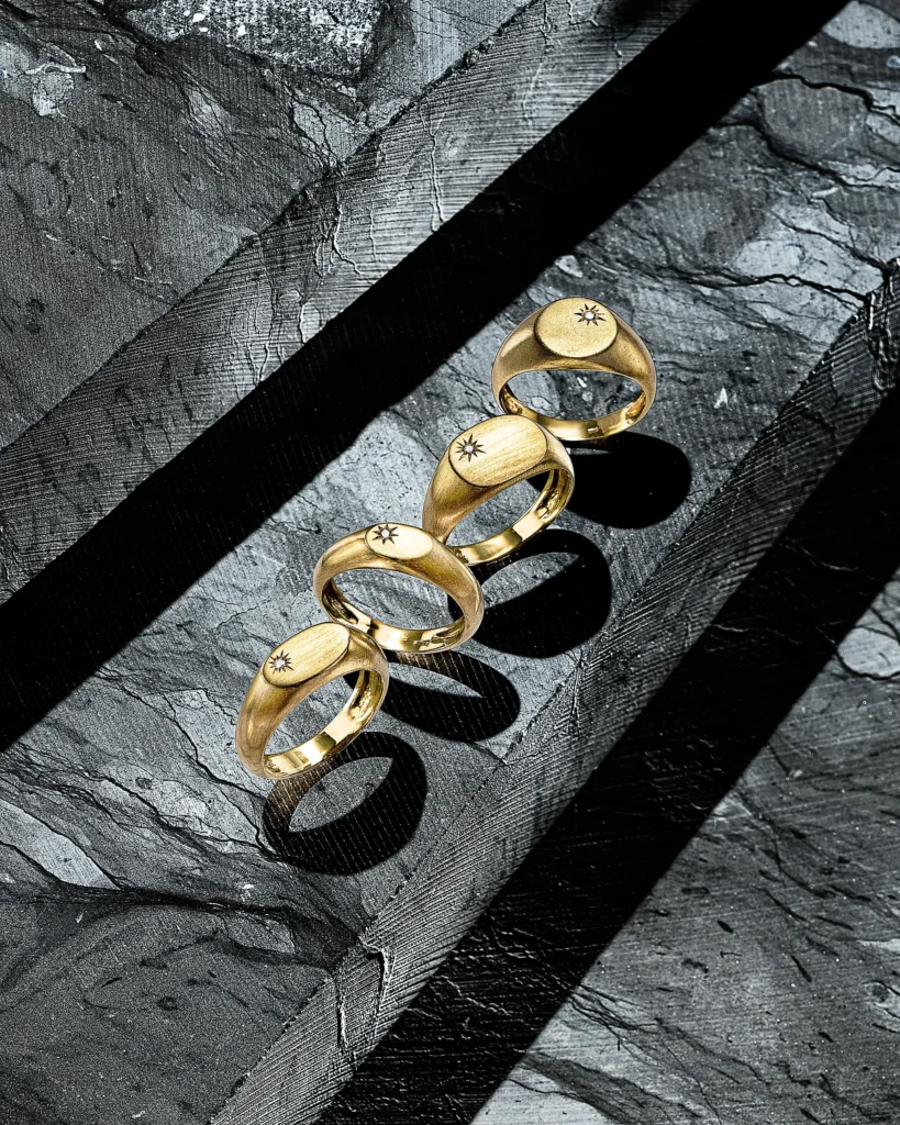 Four gold signet rings in a row on grey slate