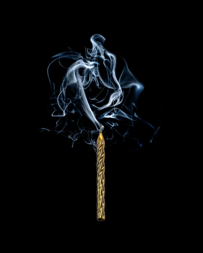 Gold match burning with a curl of blue smoke on black