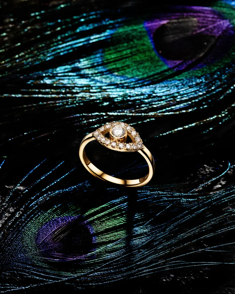 Gold ring with a diamond halo on a peacock feather