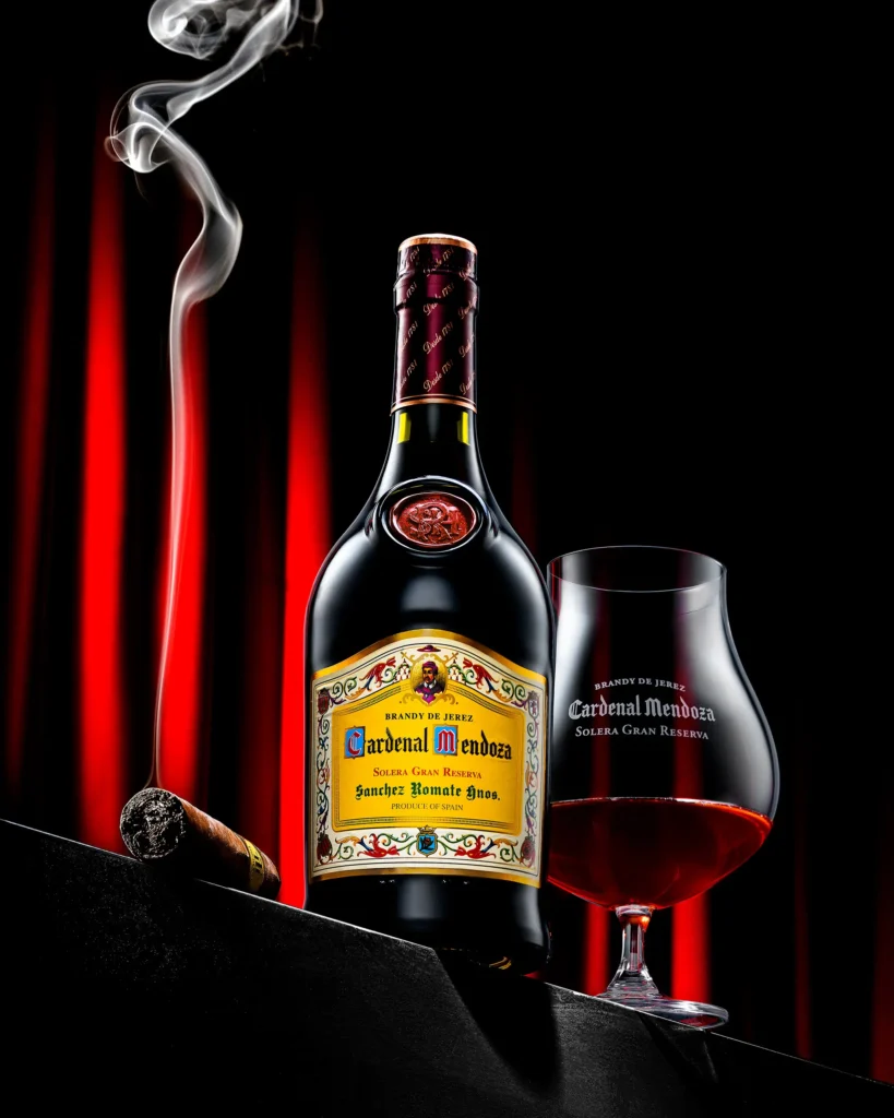 Brandy bottle, glass and cigar against a red curtain