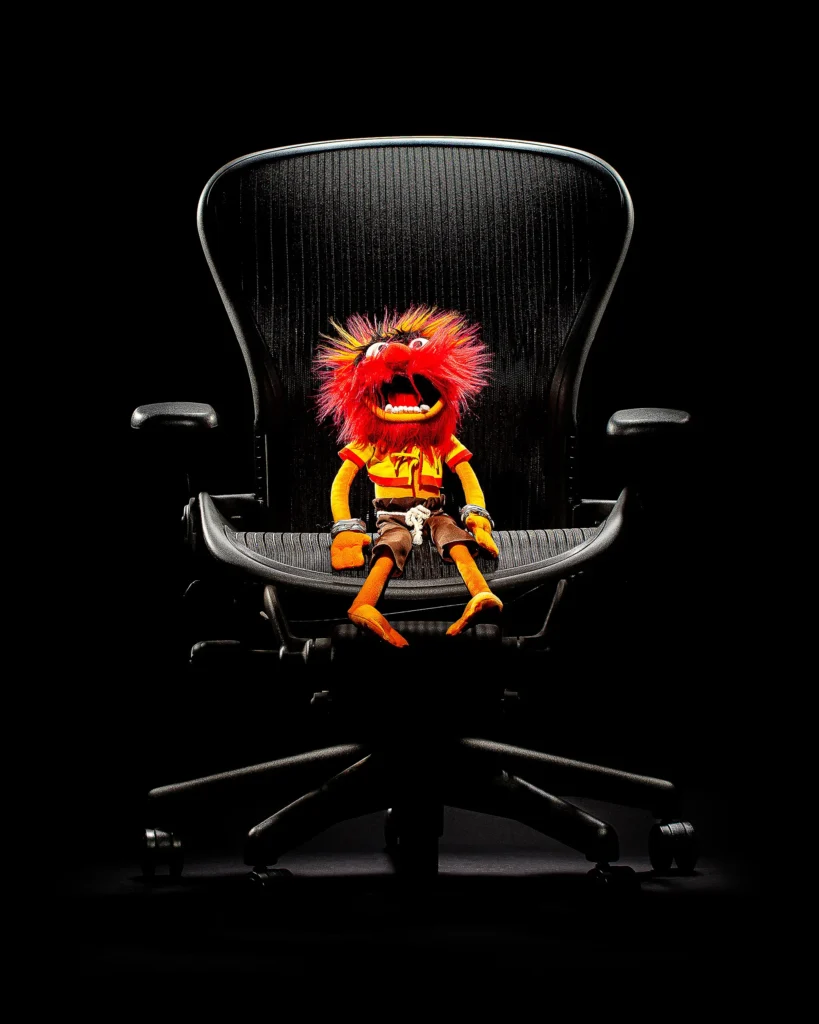 Orange puppet seated in a black mesh office chair