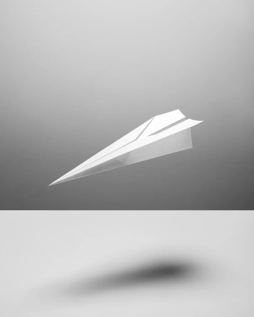 White paper plane in flight above its shadow