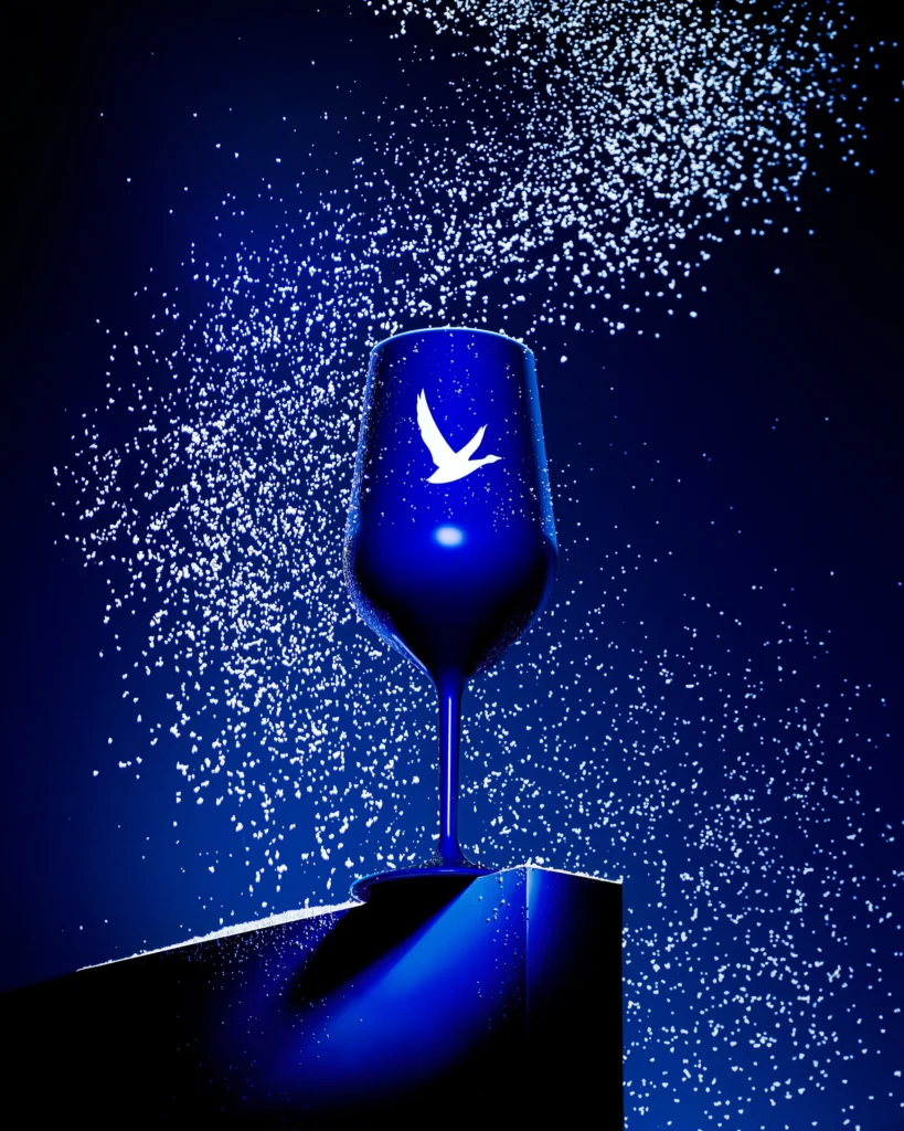 Cobalt wine glass on a white plinth under falling white particles (retouched)