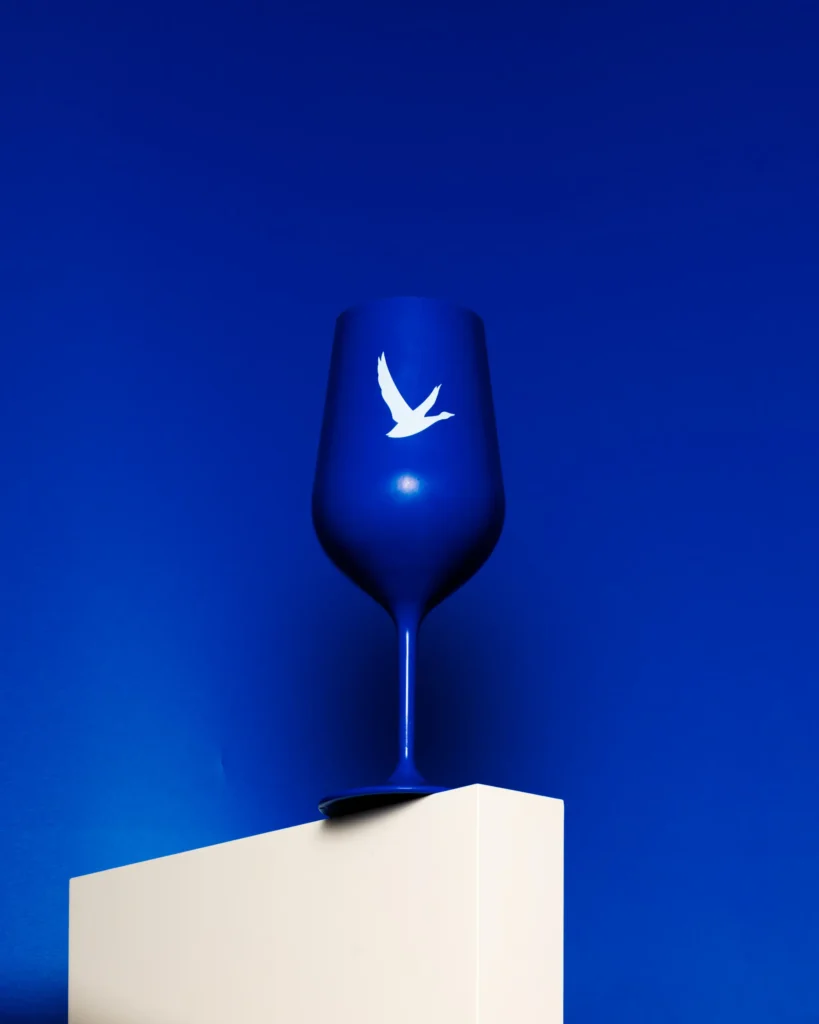 Cobalt wine glass on a white plinth under falling white particles (unretouched original)