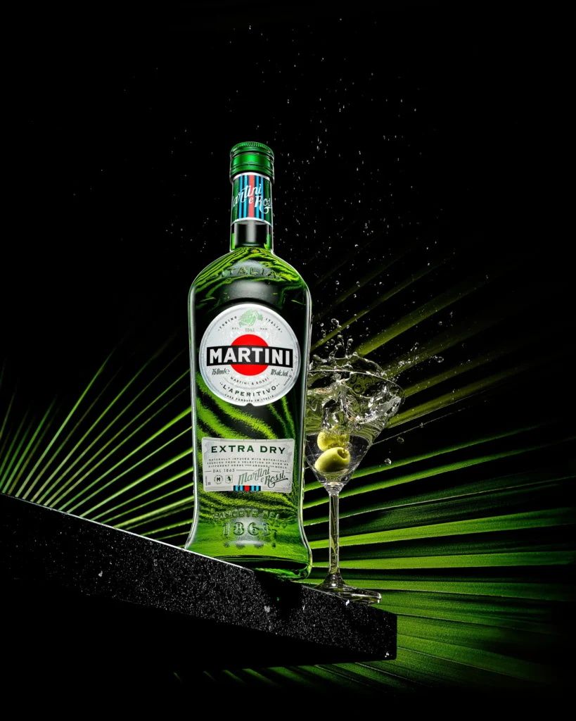 Green vermouth bottle and cocktail glass over a lit palm frond (retouched)