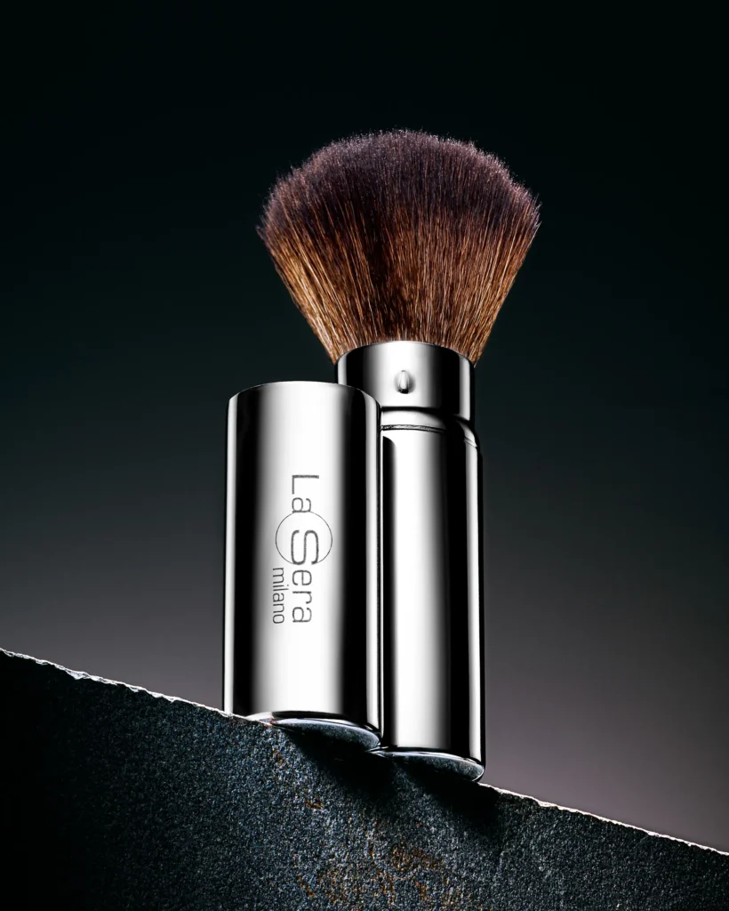 Powder brush and silver handle balanced on a dark stone edge (retouched)